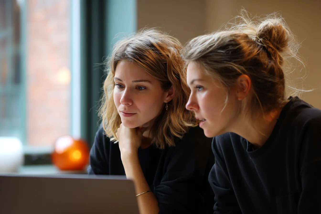 Two event planners working side by side at a laptop in a bright studio, reviewing details together.